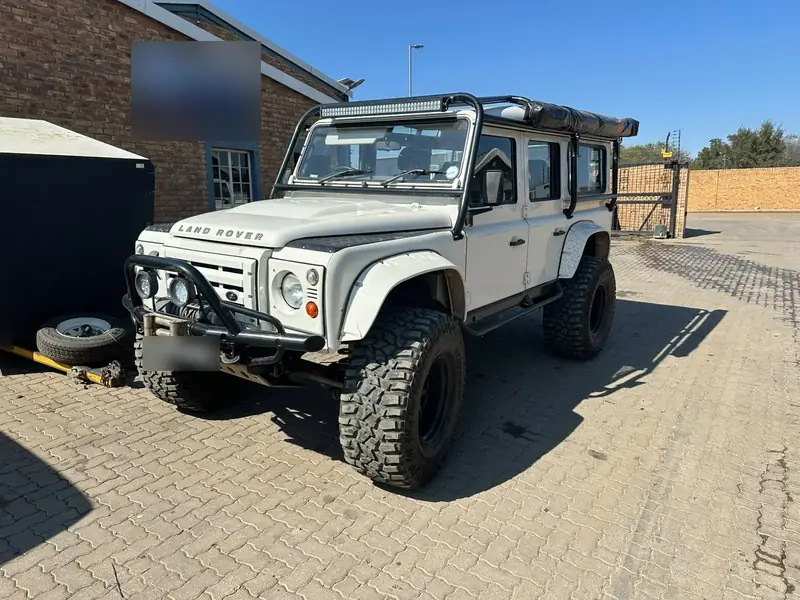 White Land Rover Defender 110 with an external roll cage, roof light bar, winch bumper, wheel-arch flares and mud-terrain tyres